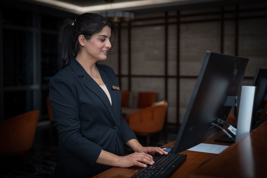 Hotel receptionist smiling at the front desk, working on a computer